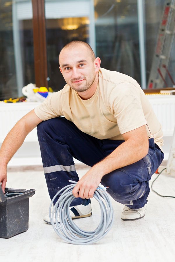 Male Worker Kneeling Down Holding Wire and Reaching into a Box